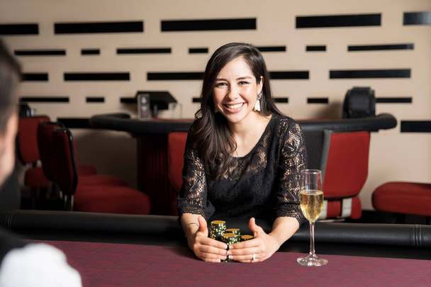 Portrait of a gorgeous Hispanic woman holding a bunch of casino chips after getting a winning hand in a poker game - Photo, Image