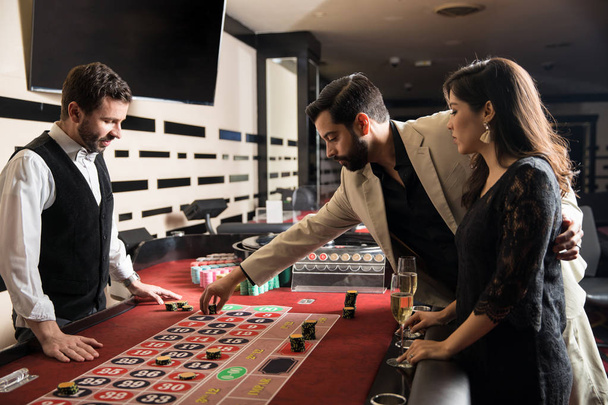 Vista de perfil de una joven pareja hispana mirando en serio y apostando en una ruleta en un casino
 - Foto, imagen