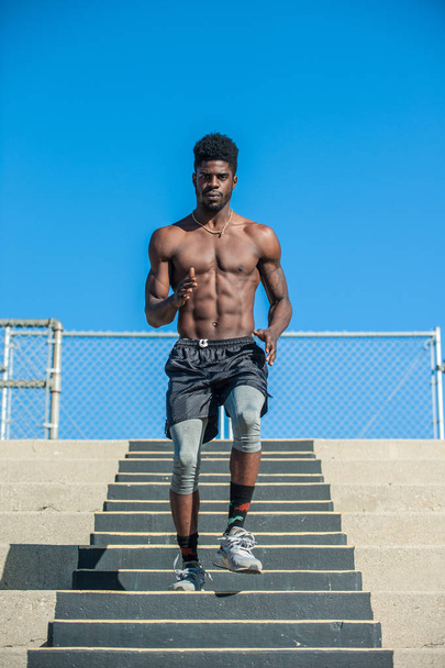 Atleta jamaicano muscular mostrando músculos abdominales rasgados mientras defiende pasos concretos durante el entrenamiento
.  - Foto, imagen