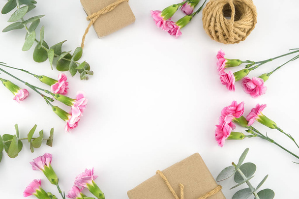 braune Geschenkboxen und Seile mit Baby-Eukalyptusblättern und rosa Nelkenblüten auf weißem Hintergrund mit Kopierraum - Foto, Bild