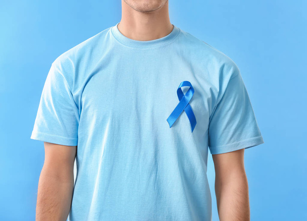 Young man wearing t-shirt with blue ribbon on color background, closeup. Prostate cancer awareness concept - Fotoğraf, Görsel
