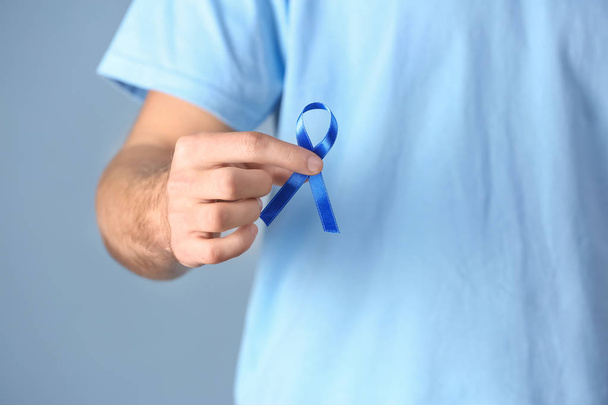 Young man holding blue ribbon on color background, closeup. Prostate cancer awareness concept - Φωτογραφία, εικόνα