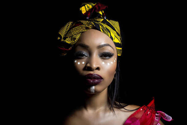 Black female showing African pride by wearing Nigerian traditional clothing and tribal makeup or face painting.  The model is shot in studio in modern vogue fashion style. - 写真・画像