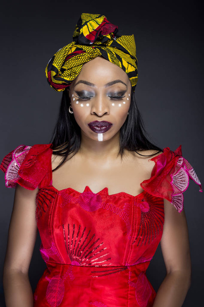 Black female showing African pride by wearing Nigerian traditional clothing and tribal makeup or face painting.  The model is shot in studio in modern vogue fashion style. - Photo, Image