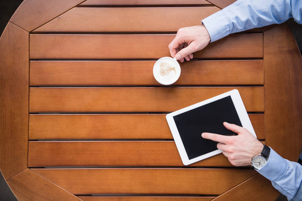 cropped image of man using tablet and holding cup of coffee - Foto, afbeelding