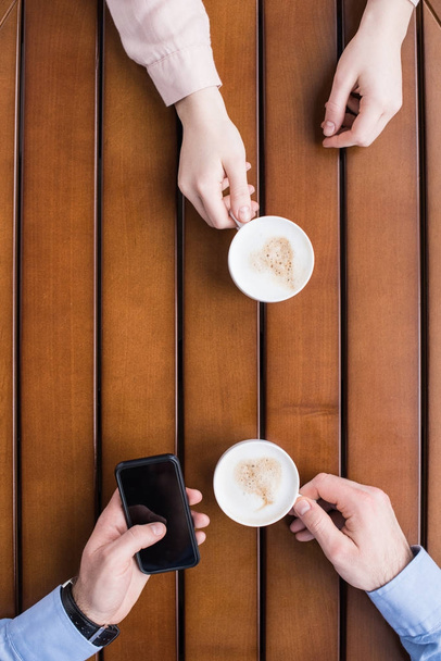 levágott kép a férfi és a nő ül a csésze kávé és ember használ smartphone - Fotó, kép