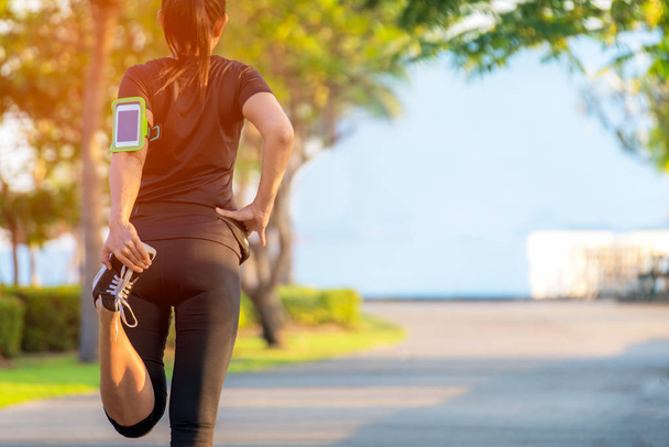 Mujer asiática de fitness corredora estirando las piernas antes de correr entrenamiento al aire libre en el parque. Concepto saludable
 - Foto, imagen