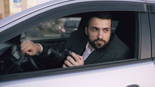 Young private detective man sitting inside car and photographing with dslr camera - Fotoğraf, Görsel