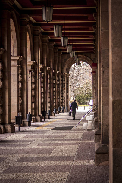 a man walks between the columns of a large old building. a tunnel formed by large columns. how small are the people to the big old buildings. - Photo, Image