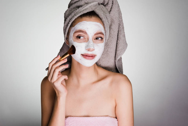 a young girl wants to look good, on her head a towel, puts on her face a white mask with a brush - 写真・画像