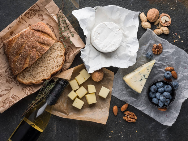 assorted cheese slices on wooden board with olive oil, blueberries ans nuts, top view  - Foto, imagen