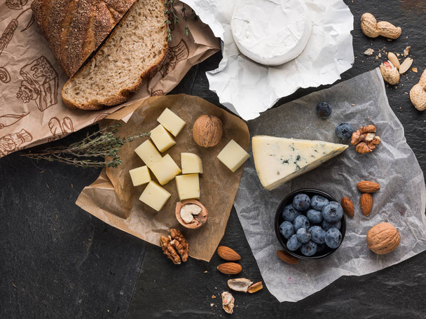 assorted cheese slices on wooden board with olive oil, blueberries and nuts on stone table with copy space - Fotó, kép