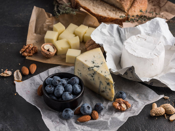 assorted cheese slices on wooden board with olive oil, blueberries and nuts, top view - 写真・画像