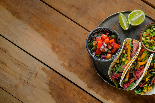 spicy tacos with lime slices and cut vegetables in bowls on wooden table, top view - Photo, Image