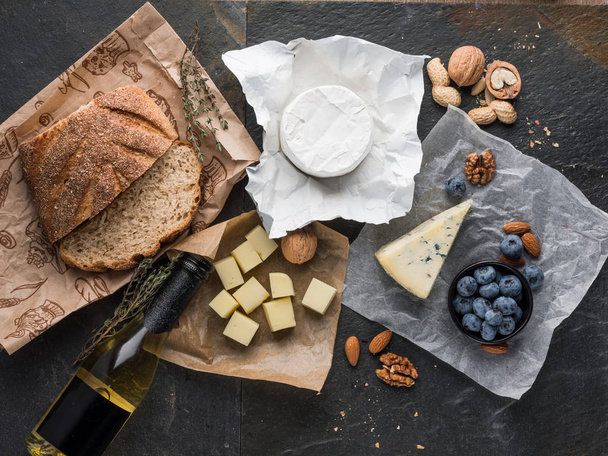 assorted cheese slices on wooden board with olive oil, blueberries ans nuts, top view  - Photo, Image