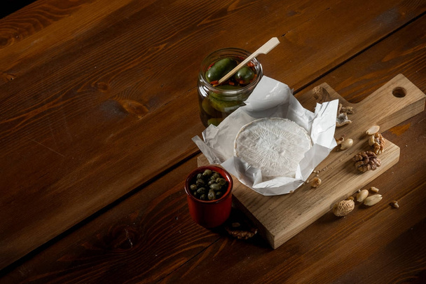 flat lay with brie cheese, nuts and jars with olives and capperi on rustic wooden table with copy space - Фото, зображення