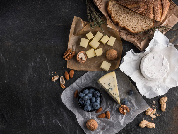 assorted cheese slices on wooden board with olive oil, blueberries and nuts on stone table with copy space - Valokuva, kuva