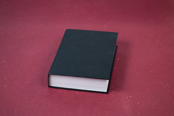 Libro de tapa dura negro cerrado grande sobre fondo rojo, superficie
. - Foto, imagen