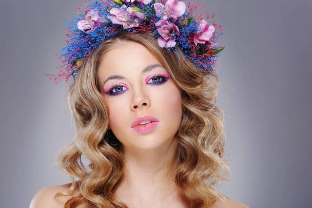 portrait of young beautiful woman wearing wreath of pink and blue flowers posing over grey background  - Foto, Bild