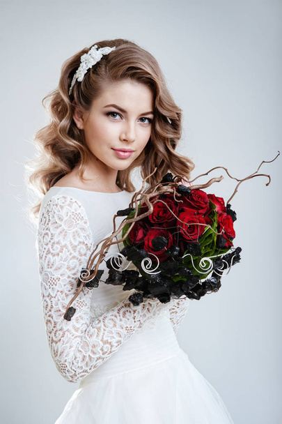 fashion portrait of young beautiful woman in white wedding dress posing with bouquet of red roses  - Fotó, kép