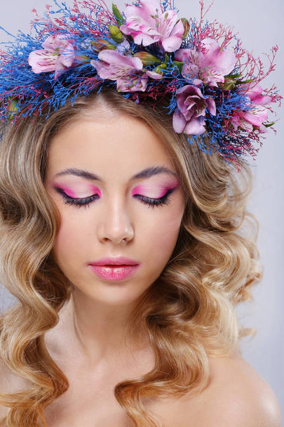 portrait of young beautiful woman wearing wreath of pink and blue flowers posing over grey background  - Foto, Imagem