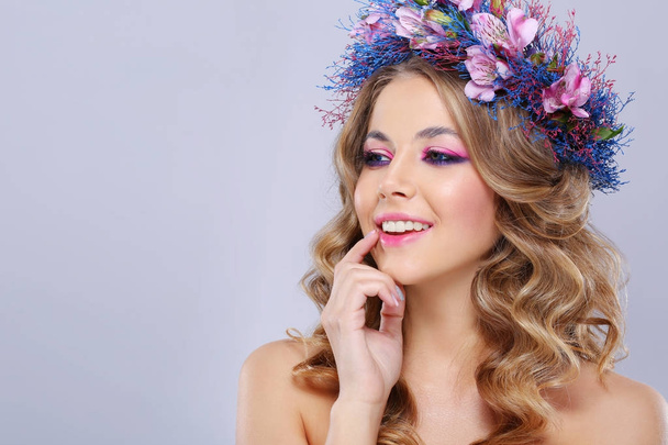 portrait of young beautiful woman wearing wreath of pink and blue flowers posing over grey background  - Foto, afbeelding