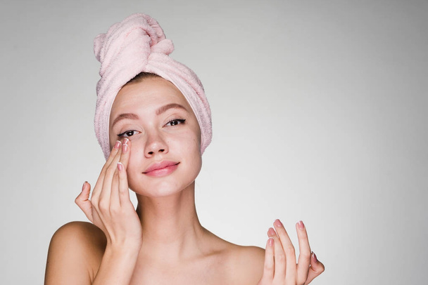 jovem atraente com toalha rosa na cabeça aplicando hidratante no rosto
 - Foto, Imagem