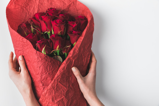 partial view of woman holding bouquet of red roses in wrapping paper for st valentines day isolated on white - Fotografie, Obrázek