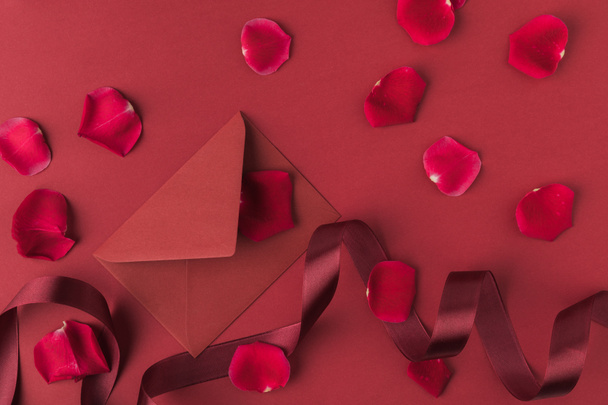 vlakke leggen met gearrangeerde rode rozen bloemblaadjes, envelop en lint geïsoleerd op rood, st Valentijnsdag concept - Foto, afbeelding