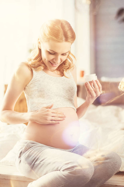 Positive pregnant woman applying body cream - Fotó, kép