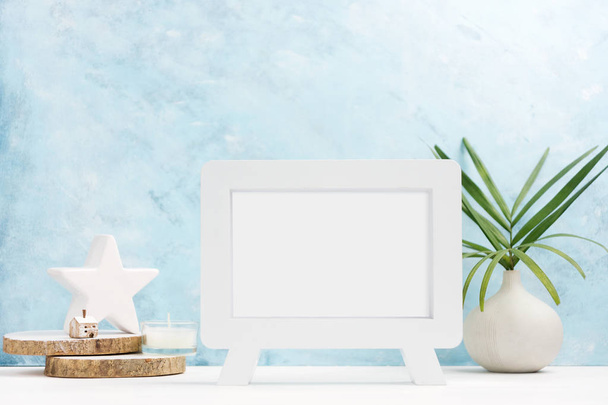 White Photo frame mock up with plants in vase, ceramic decor on shelf on blue background. Scandinavian style. Text space - Foto, afbeelding