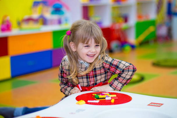 Feliz niña sonriente juega con constructor colorido en la habitación de los niños, juego de lógica, mosaico cúbico. Diseño creado por cubos. El concepto de pensamiento lógico, formas geométricas
. - Foto, imagen