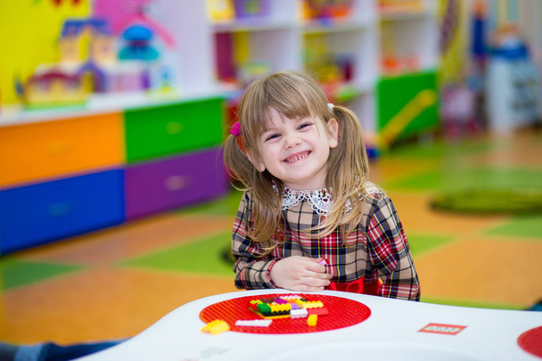 Feliz niña sonriente juega con constructor colorido en la habitación de los niños, juego de lógica, mosaico cúbico. Diseño creado por cubos. El concepto de pensamiento lógico, formas geométricas
. - Foto, imagen