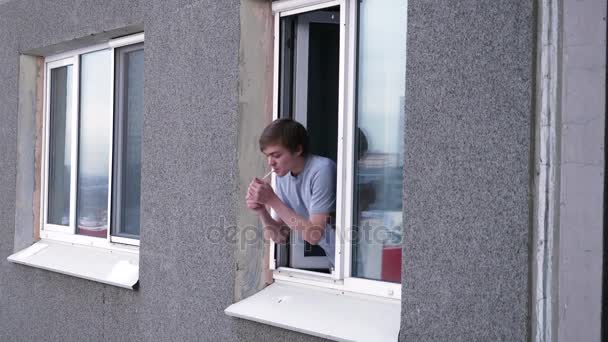 Młody człowiek rozmowy z sasiadem przez okno. Młody człowiek pali papierosa i rozmowy z sąsiadem z jego okna - Materiał filmowy, wideo