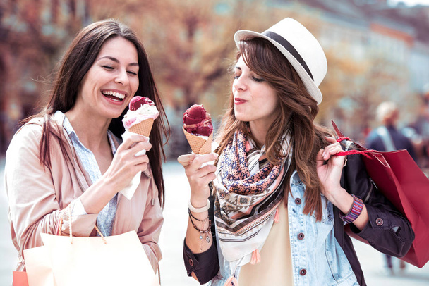 Mooie stijlvolle meisjes is ijs eten, praten en lachen tijdens het wandelen na het winkelen. - Foto, afbeelding