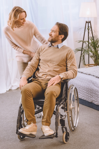 happy husband on wheelchair and wife looking at each other - Фото, изображение