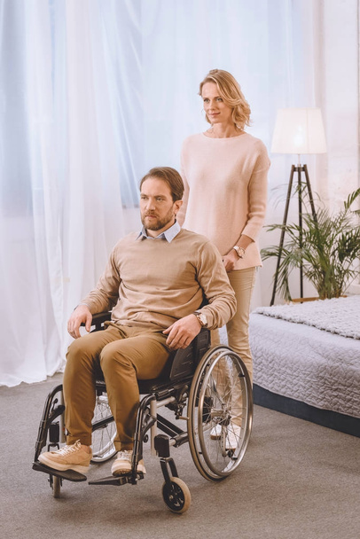 husband on wheelchair and wife looking away in bedroom - Foto, imagen