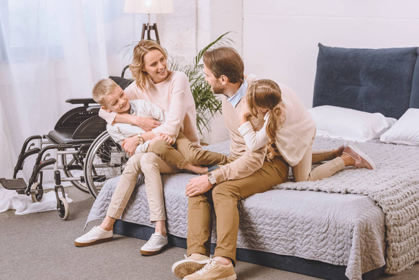 padre con discapacidad y madre feliz sentado con los niños en la cama
 - Foto, Imagen