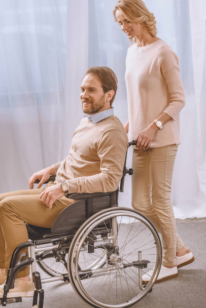 wife carrying happy husband in wheelchair - Foto, imagen