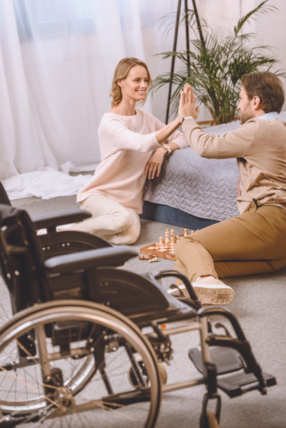 marido con discapacidad y esposa jugando al ajedrez en el dormitorio y dando cinco
 - Foto, Imagen