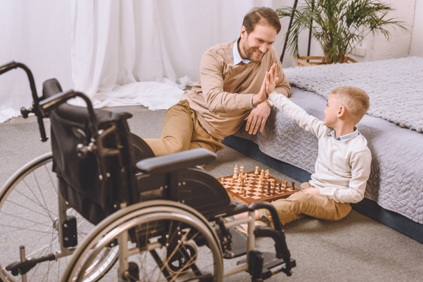 father with disability and son playing chess and giving high five - Fotoğraf, Görsel