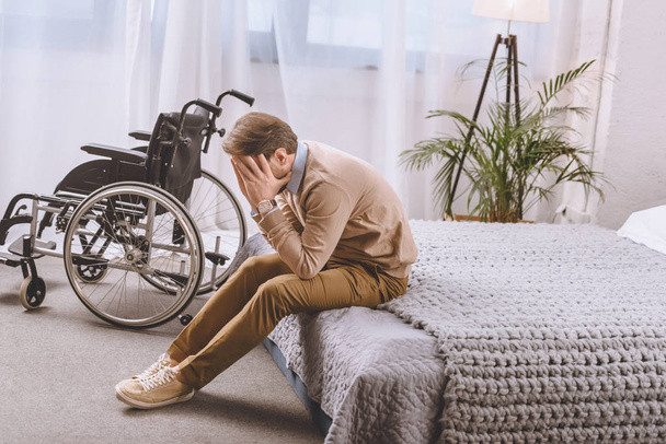 upset man with disability sitting on bed and covering face with hands - Foto, afbeelding