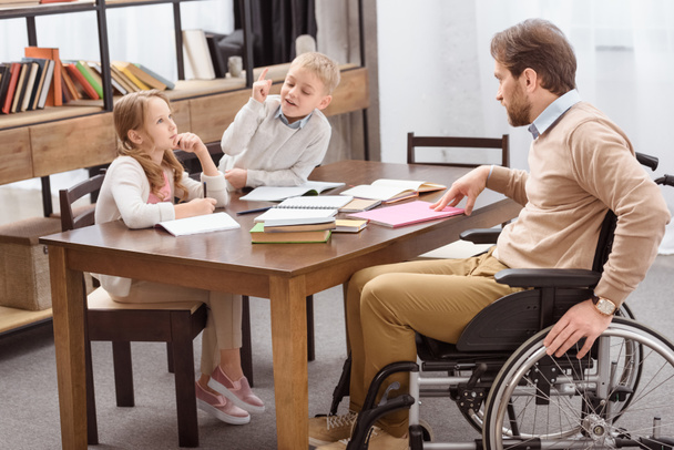 father on wheelchair helping kids with education at home - Foto, Imagen