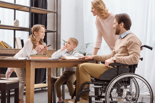 smiling father on wheelchair and mother teaching children at home - Foto, Bild