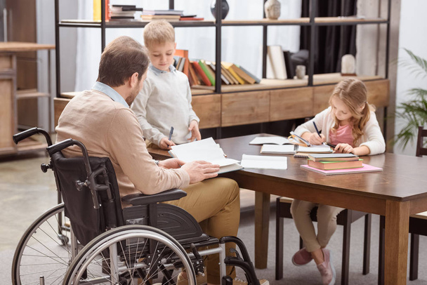father on wheelchair helping kids with education at home - Valokuva, kuva