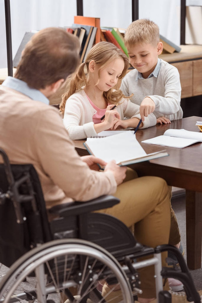 pai em cadeira de rodas ensinando crianças em casa
  - Foto, Imagem