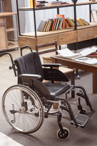 Leerer Rollstuhl am Tisch mit Notizbüchern im Zimmer - Foto, Bild