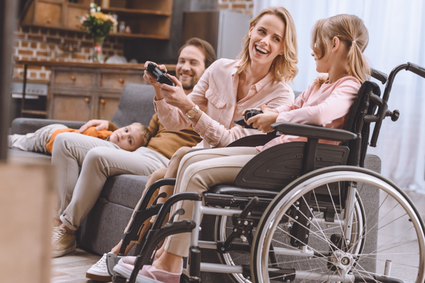 οικογένεια με ανάπηρο παιδί στην αναπηρική καρέκλα που παίζει με χειριστήρια μαζί στο σπίτι  - Φωτογραφία, εικόνα