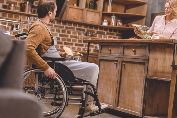 selective focus of woman with disabled man in wheelchair cooking dinner together at home   - Foto, afbeelding