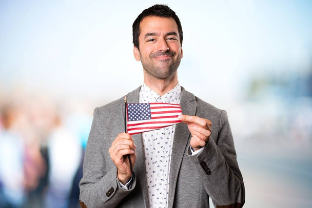 やり場のない背景にアメリカの国旗を持って幸せなハンサムな男 - 写真・画像
